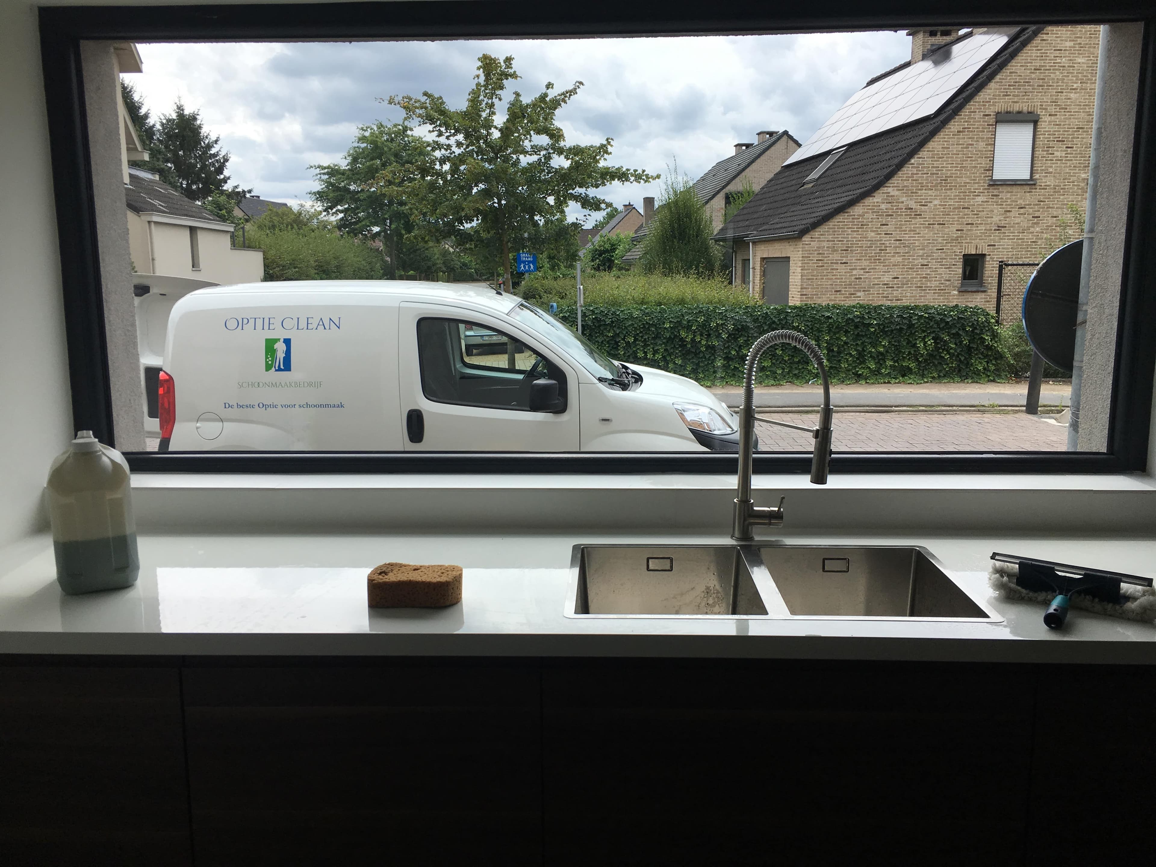 Évier de cuisine devant une fenêtre montrant une camionnette blanche et des maisons voisines.